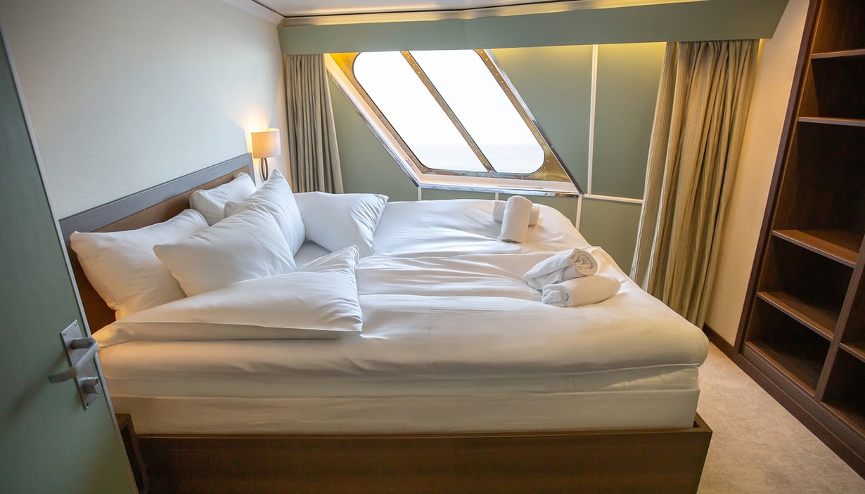 Lugar med pent oppredd seng, vindu og håndklesvaner.