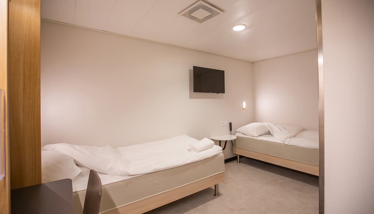 Tilgjengelig lugar med to enkeltsenger og et rundt bord.