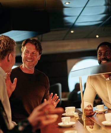 Gruppe mennesker samlet ved en kafédisk som nyter kaffe og samtale