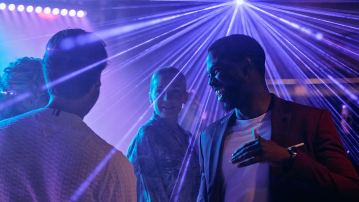 Gruppe mennesker som snakker på fest med fargerik belysning.