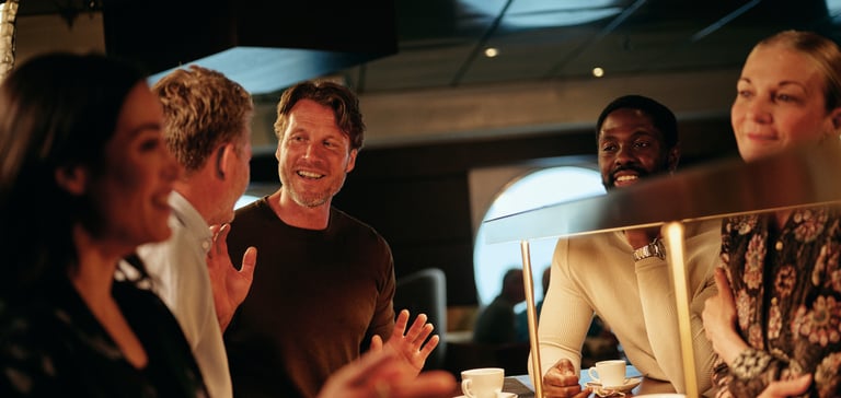 Gruppe mennesker samlet ved en kafédisk som nyter kaffe og samtale