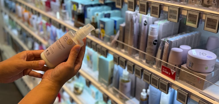 Person holder en hudpleieflaske i en butikkgang med skjønnhetsprodukter