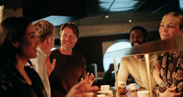 Gruppe mennesker samlet ved en kafédisk som nyter kaffe og samtale