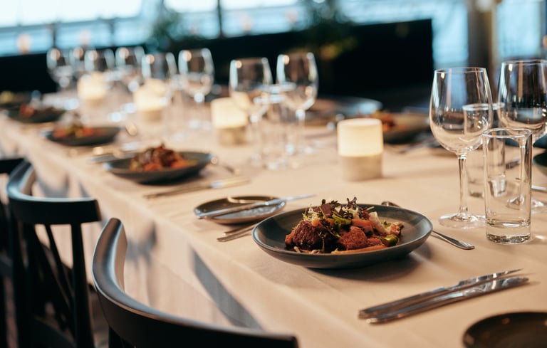 Elegant dekket spisebord med hvit duk, salat, bestikk, stearinlys og vinglass