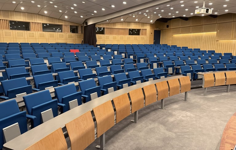 Tomt auditorium med blå stoler og trepulter