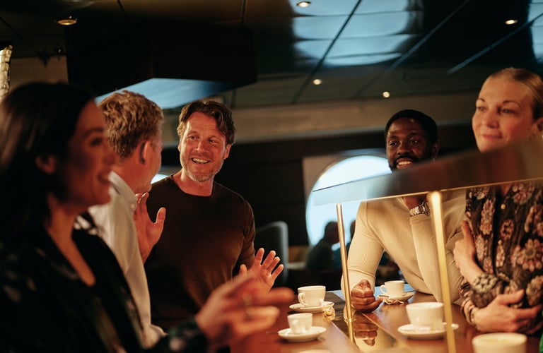 Gruppe mennesker samlet ved en kafédisk som nyter kaffe og samtale